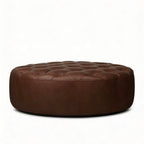 Moroccan Leather Pouf Dark Brown leather ottoman in a living room setting with a beige sofa and plant.