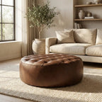 Moroccan Leather Pouf Dark Brown leather ottoman in a living room setting with a beige sofa and plant.